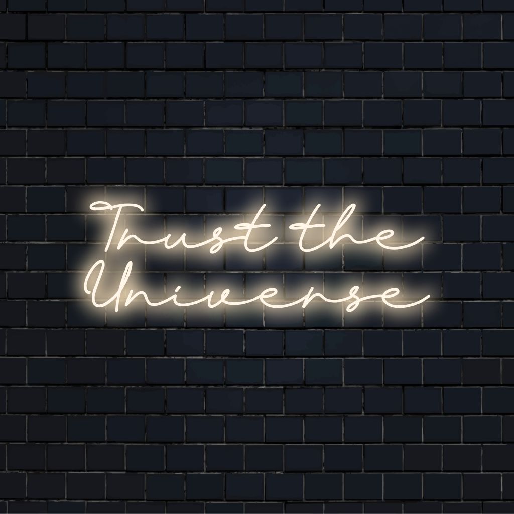 Trust The Universe Neon Light with bright neon lettering on dark brick wall