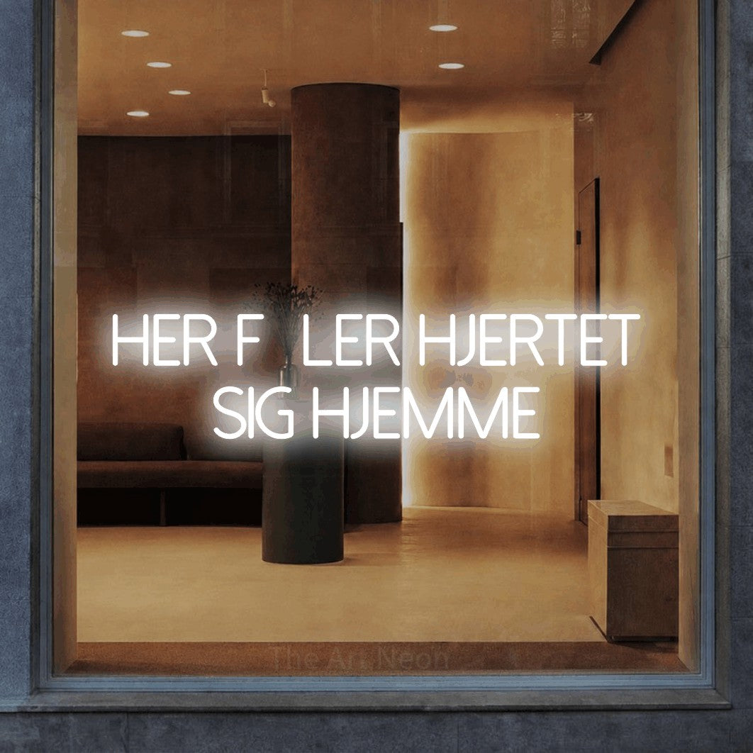 LED neon sign reading “HER føler hjertet sig hjemme”, arranged in 2 lines.