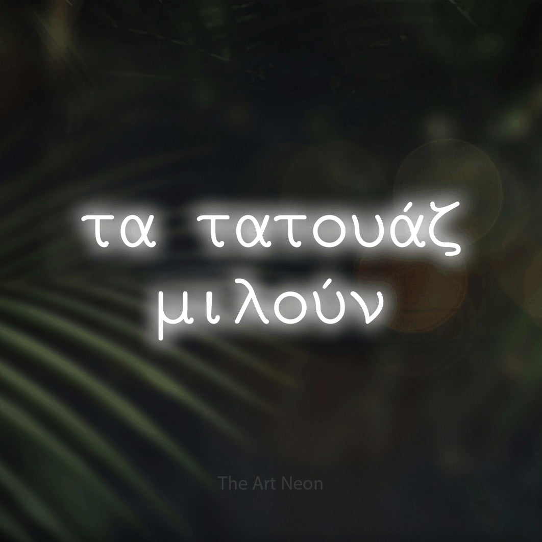 LED neon sign reading “τα τατουάζ μιλούν”, arranged in two lines.