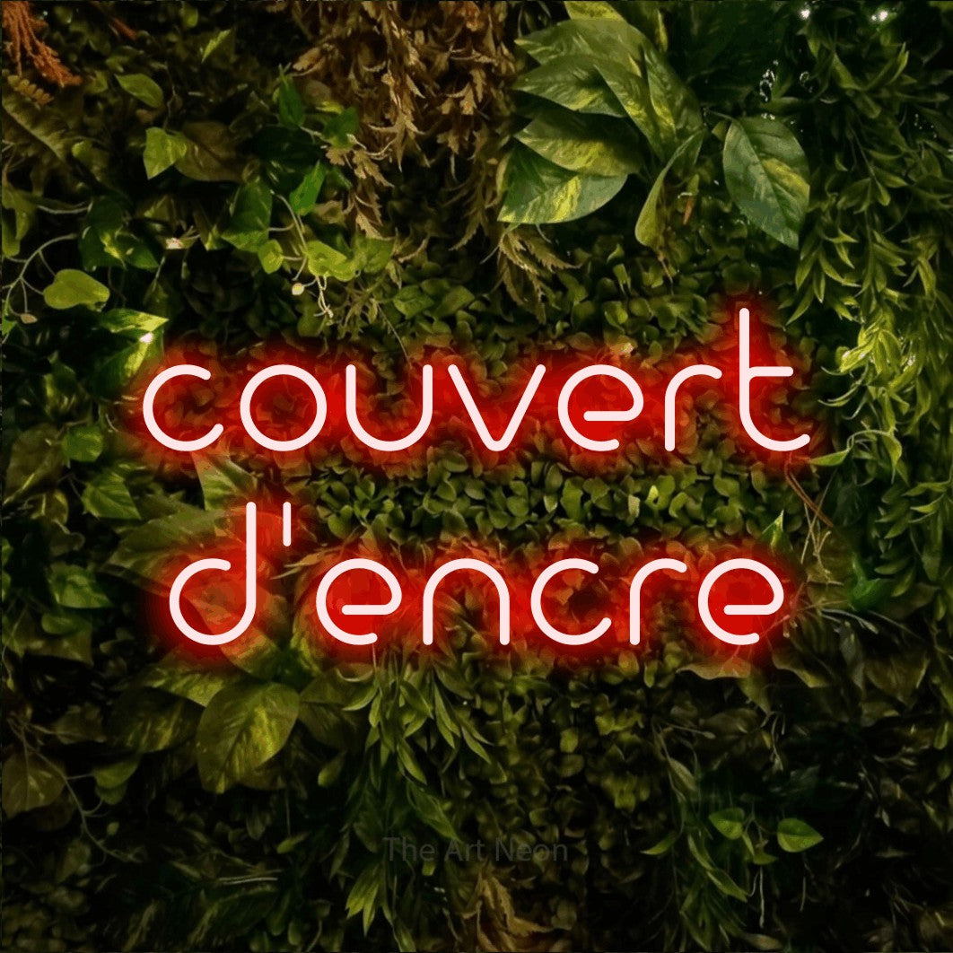 LED neon sign reading “couvert d'encre”, arranged in 2 lines.