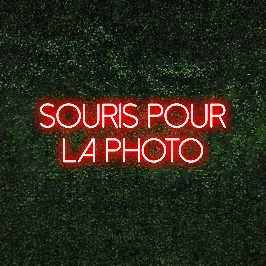 LED neon sign reading “souris pour la photo”, arranged in 2 lines.