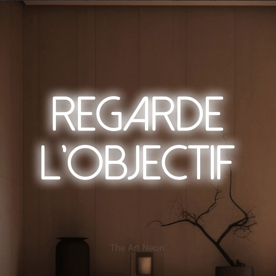 LED neon sign reading “Regarde l'objectif”, arranged in 2 lines.
