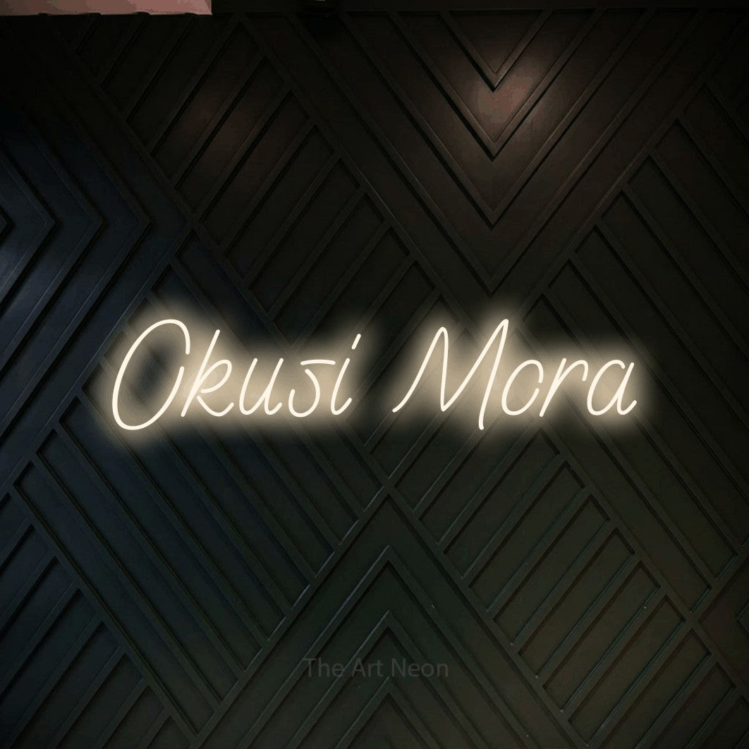 LED neon sign reading “Okusi Mora”, arranged in a single line.