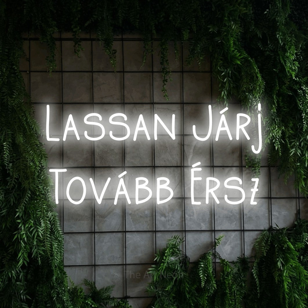 LED neon sign reading “Lassan Járj Tovább Érsz”, arranged in two lines.
