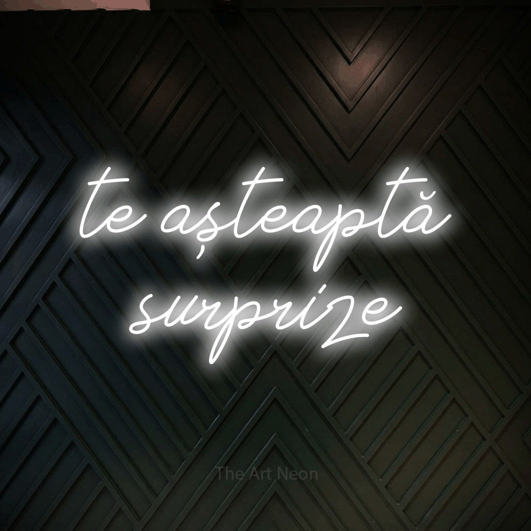 LED neon sign reading “te așteaptă surprize”, arranged in two lines.