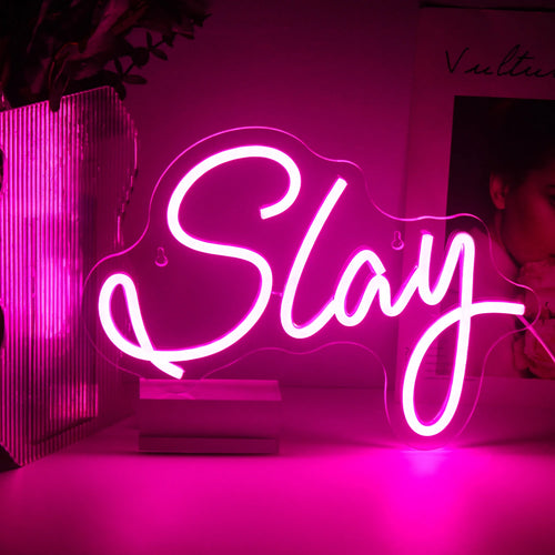 Imaginea prezintă o pancartă LED neon vibrantă, realizată manual, care afișează cuvântul „Slay” într-un font elegant, cursiv.