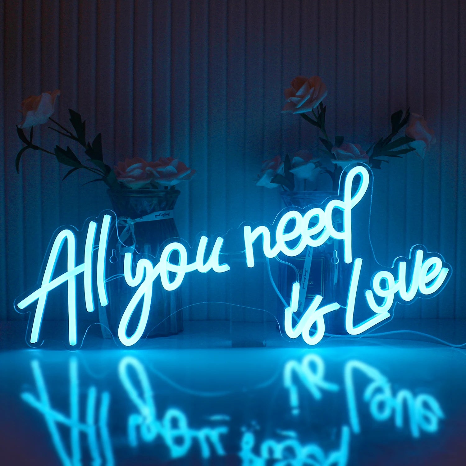 The image displays a vibrant LED neon sign that spells out the phrase "All You Need Is Love" in a stylish, cursive font.