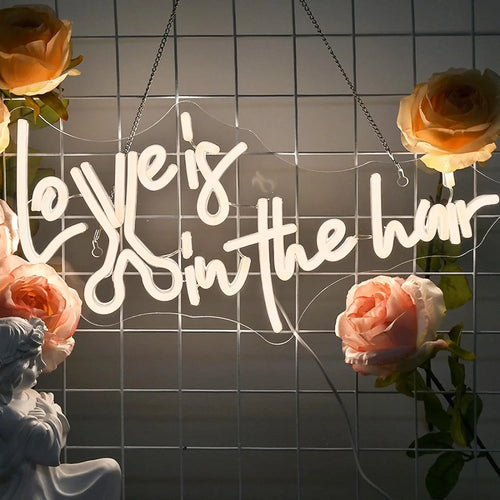 Billedet har et levende, håndlavet LED-neonskilt, der staver sætningen "Love is in the Hair.
