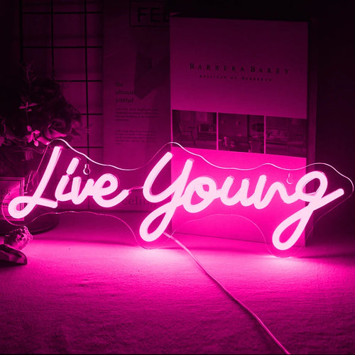 Slika prikazuje živahni ručno rađeni LED neonski znak s izrazom "Live Young" na živopisnom, kurzivnom pismu.