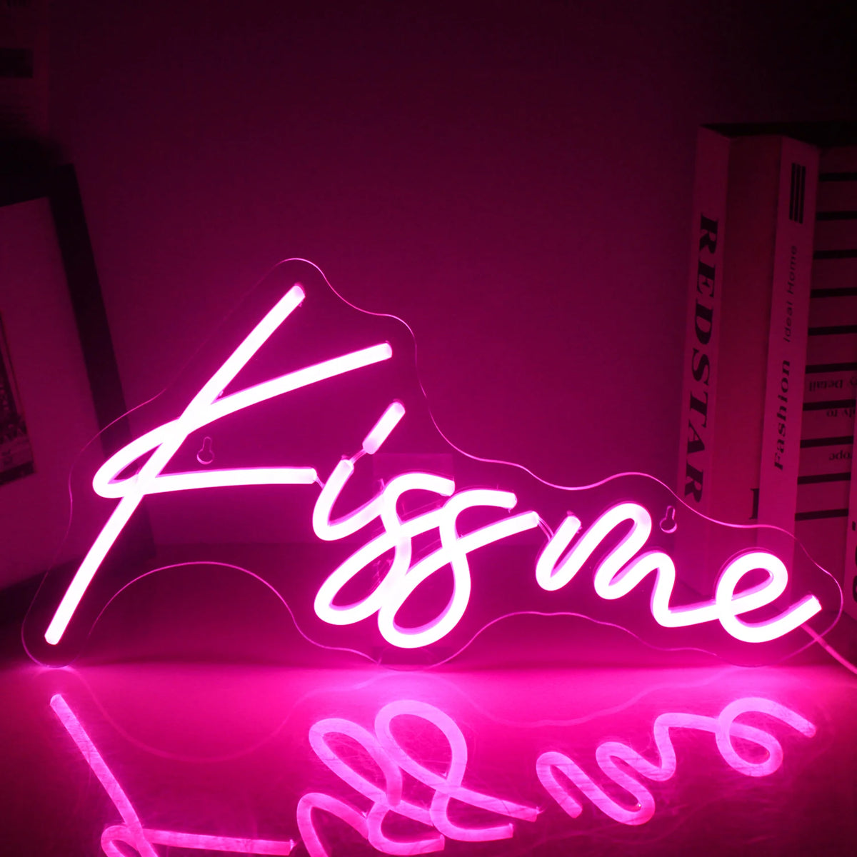 Elav "Kiss Me" LED-neoonsilt on valgustatud, kuvades tumedal taustal ereda ja julge roosa kirja.