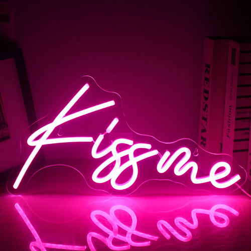 Un panou luminos cu neon LED „Kiss Me” este iluminat, afișând litere roz strălucitoare și îndrăznețe pe un fundal întunecat.