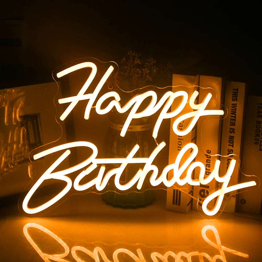 A vibrant "Happy Birthday" LED neon sign illuminates against a dark background.