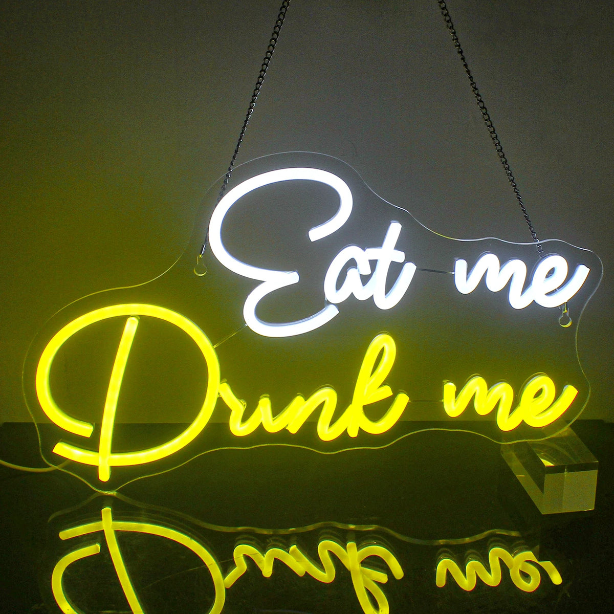 L'image présente un panneau néon LED vibrant affichant les mots « Eat Me Drink Me » dans une police cursive fantaisiste.
