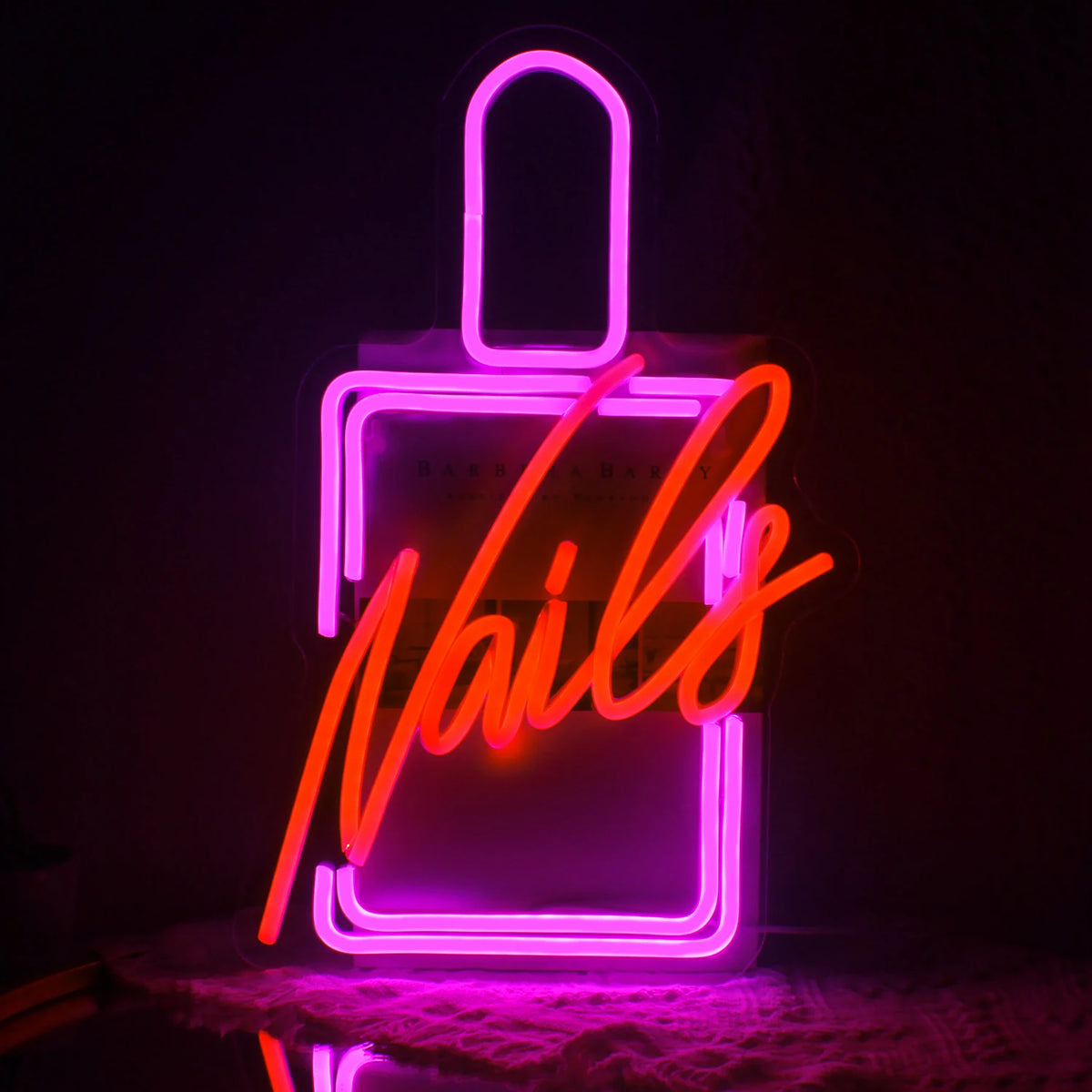 L'image présente un panneau néon LED vibrant qui énonce le mot « Nails » dans une police cursive élégante.