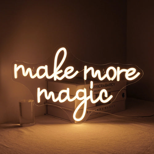 Un vibrante letrero de neón LED "Make More Magic" en una animada combinación de colores está montado sobre un fondo oscuro y elegante.