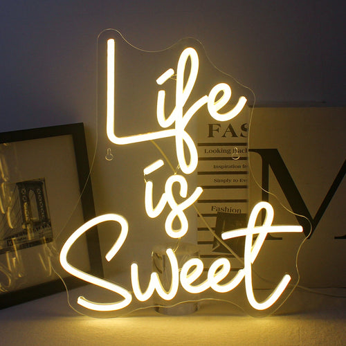 L'image présente un panneau néon LED vibrant, fait à la main, aux couleurs vives et éclatantes qui énonce la phrase « La vie est douce ».