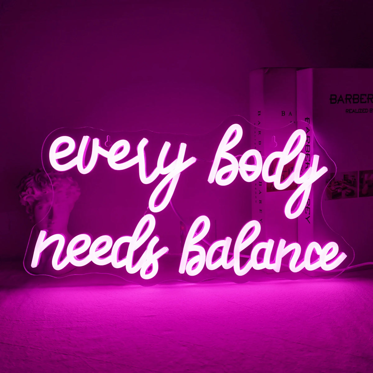 The image displays a vibrant "Every Body Needs Balance" LED neon sign.