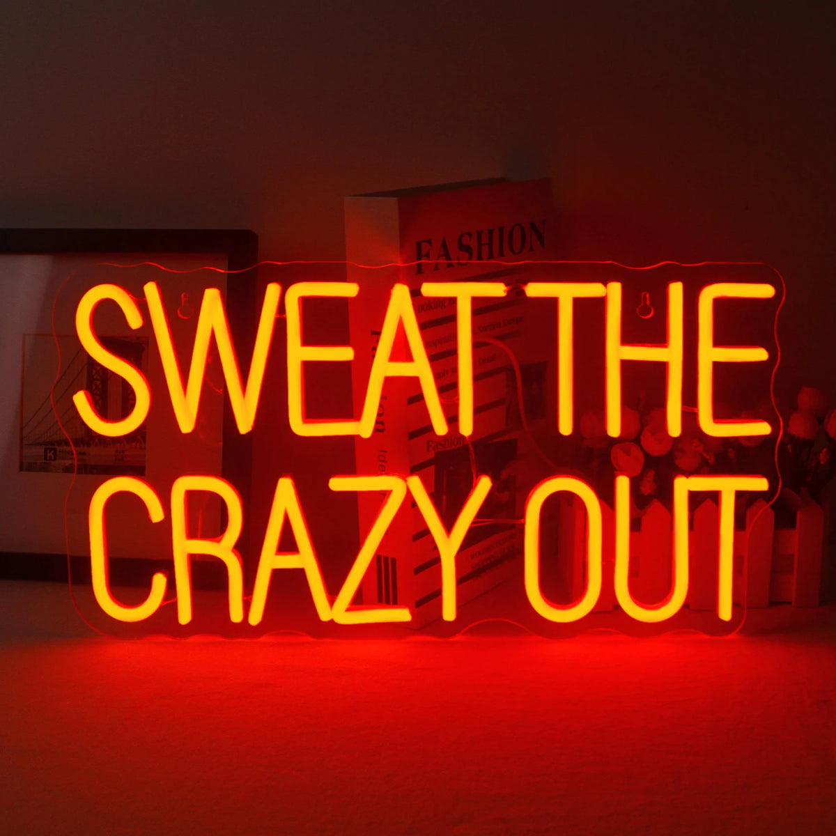 Živý neonový nápis LED zobrazující frázi „Sweat The Crazy Out“ hravým kurzívou.