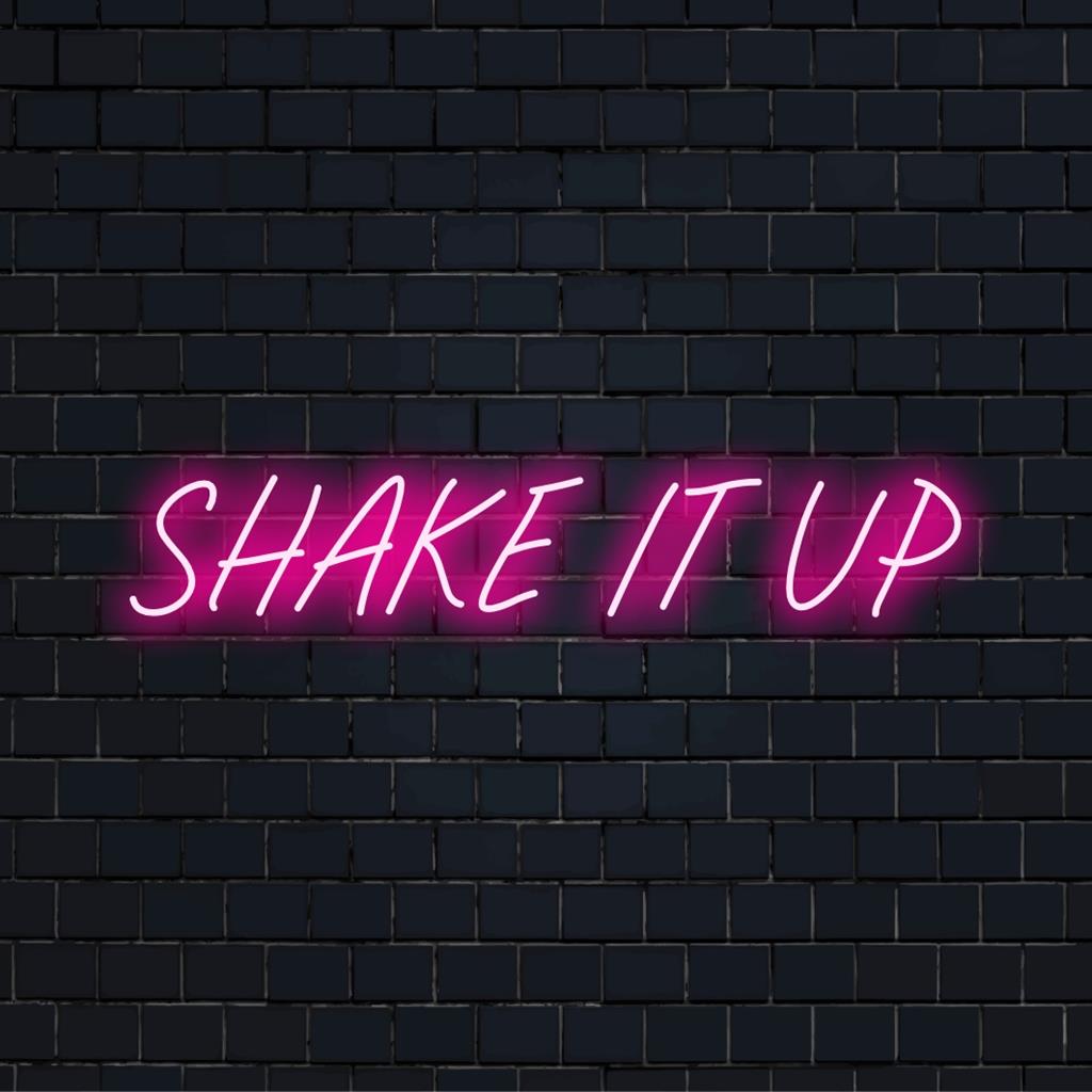 Energisk orange og pink LED-neonskilt med ordene Shake It Up, der inkarnerer levende energi og festånd.