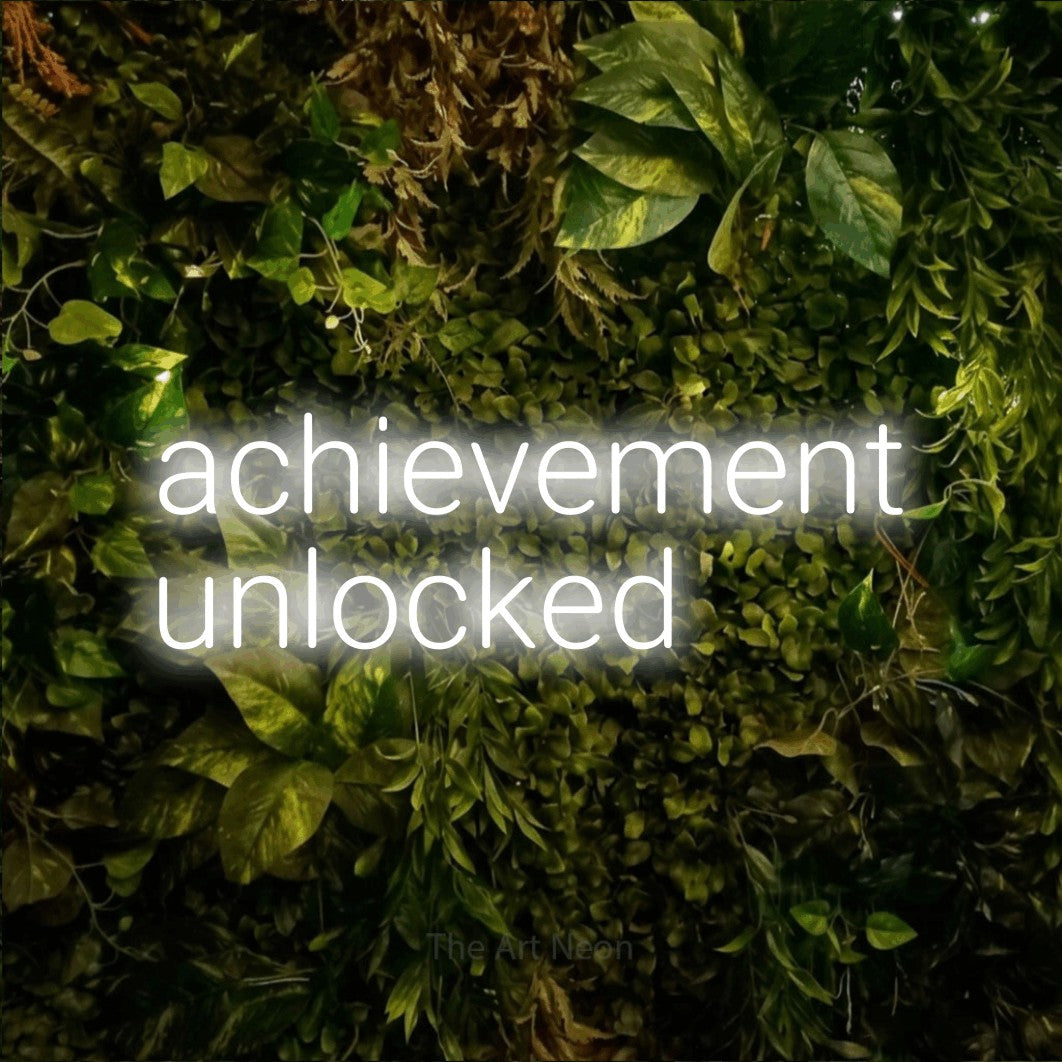 LED neon sign reading “achievement unlocked”, arranged in two lines.