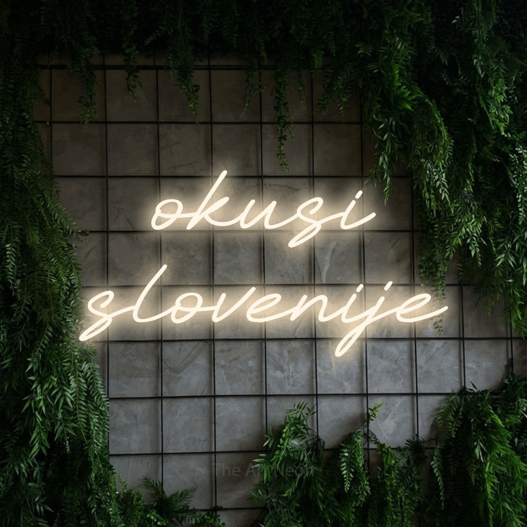 LED neon sign reading “okusi slovenije”, arranged in two lines.