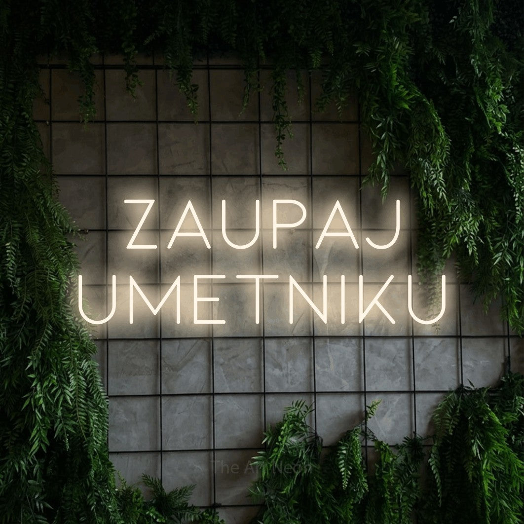 LED neon sign reading “Zaupaj UMETNIKU”, arranged in two lines.