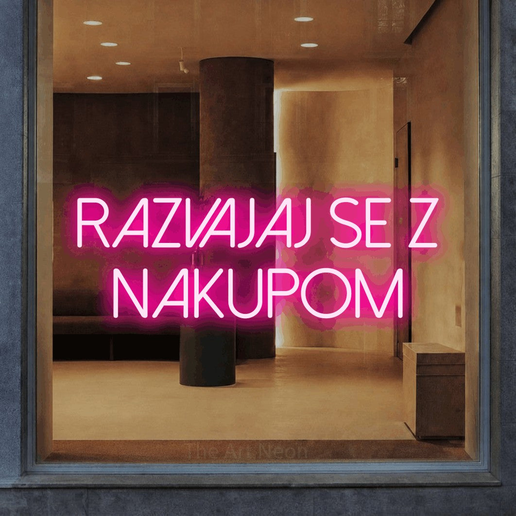 LED neon sign reading “razvajaj se z nakupom”, arranged in two lines.