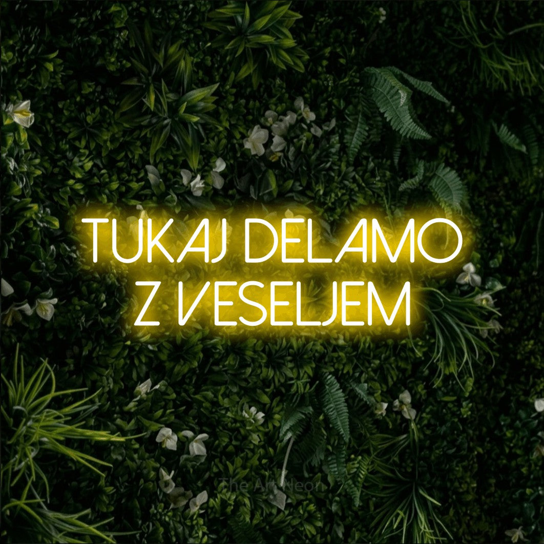 LED neon sign reading “Tukaj delamo z veseljem”, arranged in two lines.