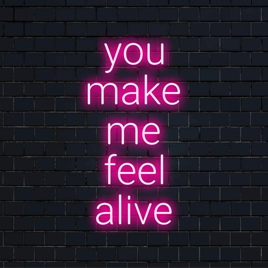 Vlastní LED neonový nápis You Make Me Feel Alive tučným písmem, zářící v zářivých barvách na tmavém pozadí.