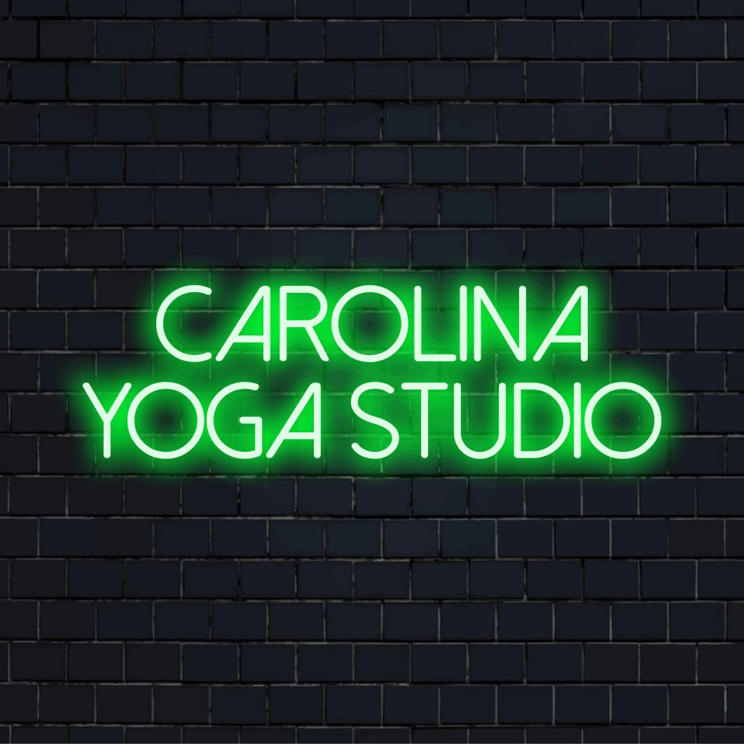 Carolina Yoga Studio Personalized Neon Light with bright neon lettering against black brick wall