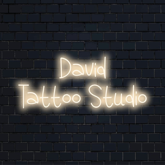 David Tattoo Studio Custom Name Neon Sign, soft neon glow against black brick wall