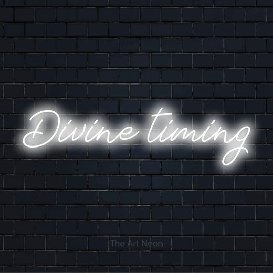 "Divine Timing" glowing LED neon sign on a black brick wall