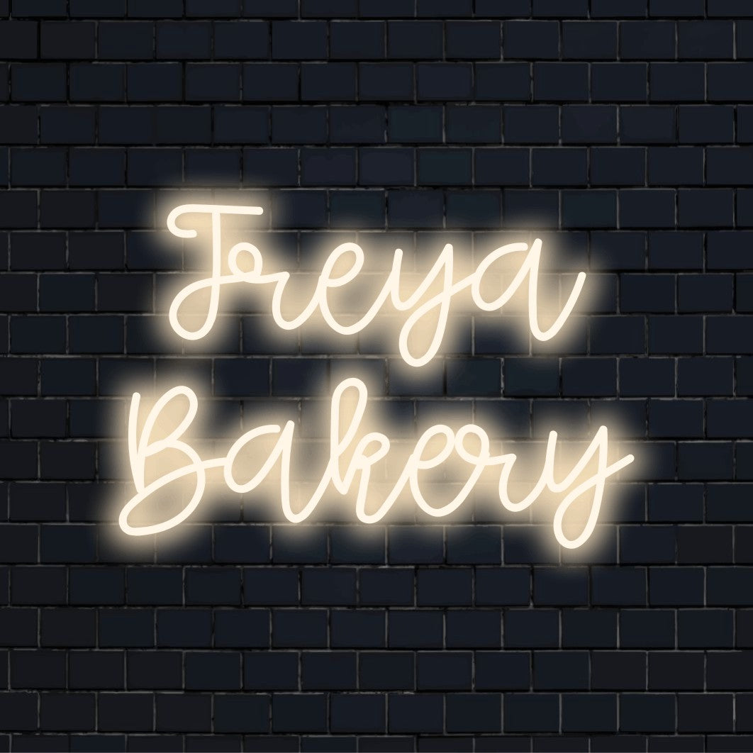 Freya Bakery Custom Name Neon Sign, bright neon lettering on dark brick background