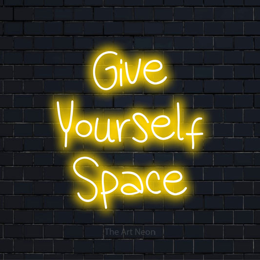 "Give Yourself Space" script-style LED neon sign on a black brick wall