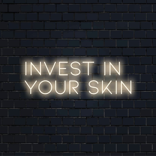 Invest In Your Skin Neon Sign, bright neon glow on black brick background