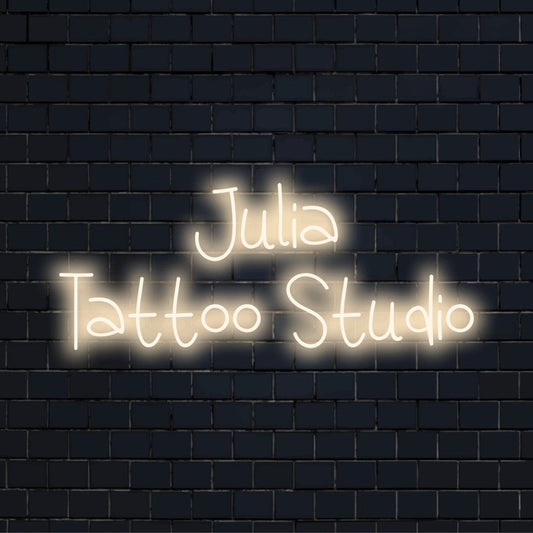 Julia Tattoo Studio Custom Name Neon Sign, glowing lettering on dark brick wall