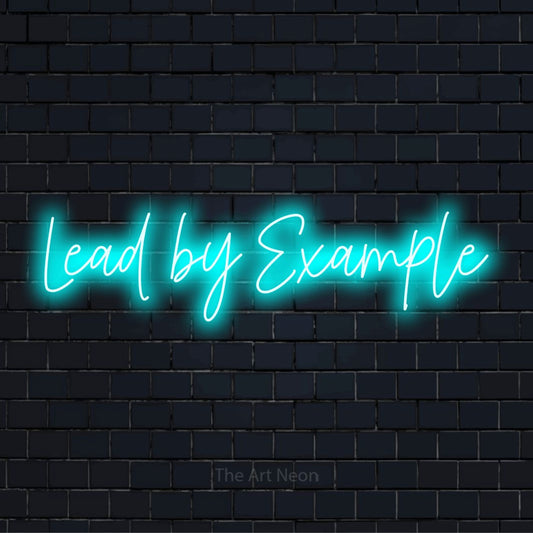 "Lead By Example" script-style LED neon sign on a black brick wall