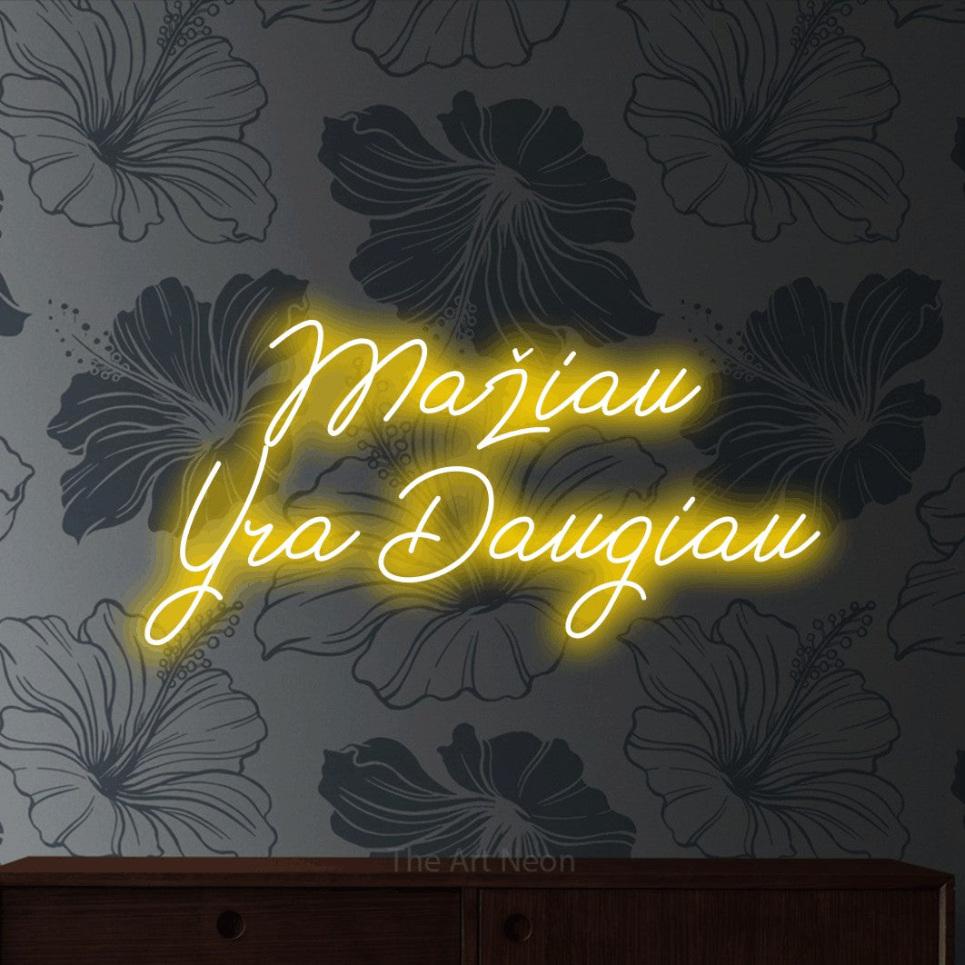 LED neon sign reading “Mažiau Yra Daugiau”, arranged in two lines.