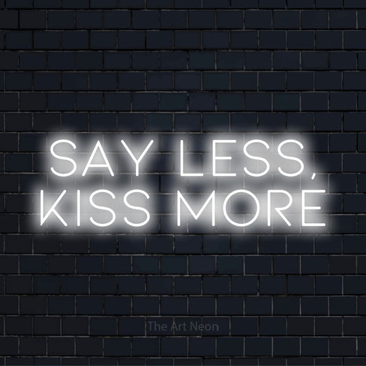 "Say Less, Kiss More" script-style LED neon sign on a black brick wall