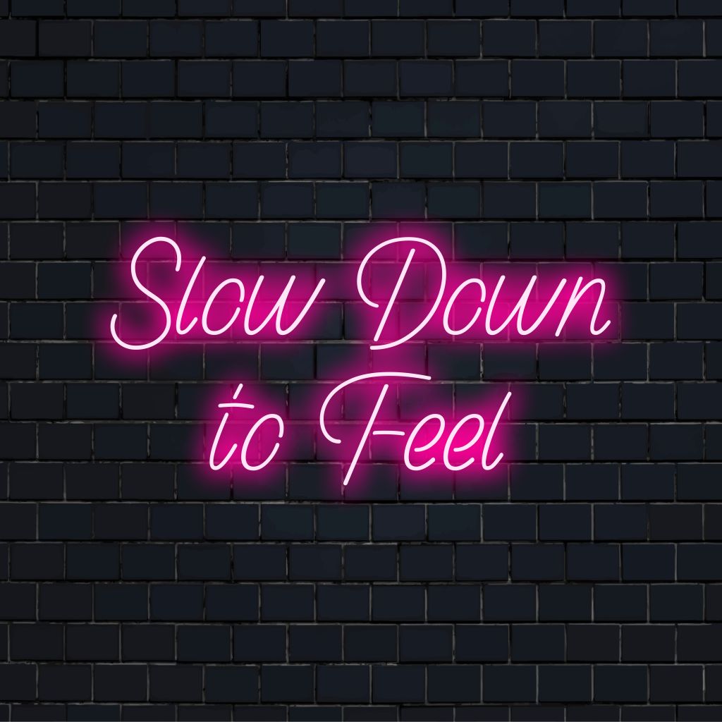 Slow Down To Feel Neon Sign, soft neon glow on dark brick wall
