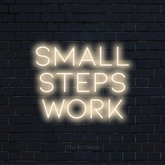 "Small Steps Work" script-style LED neon sign on a black brick wall