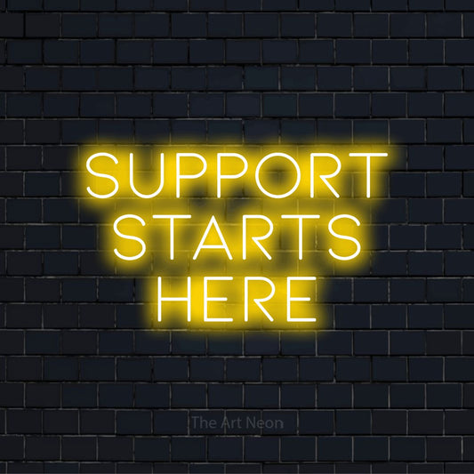 "Support Starts Here" script-style LED neon sign on a black brick wall