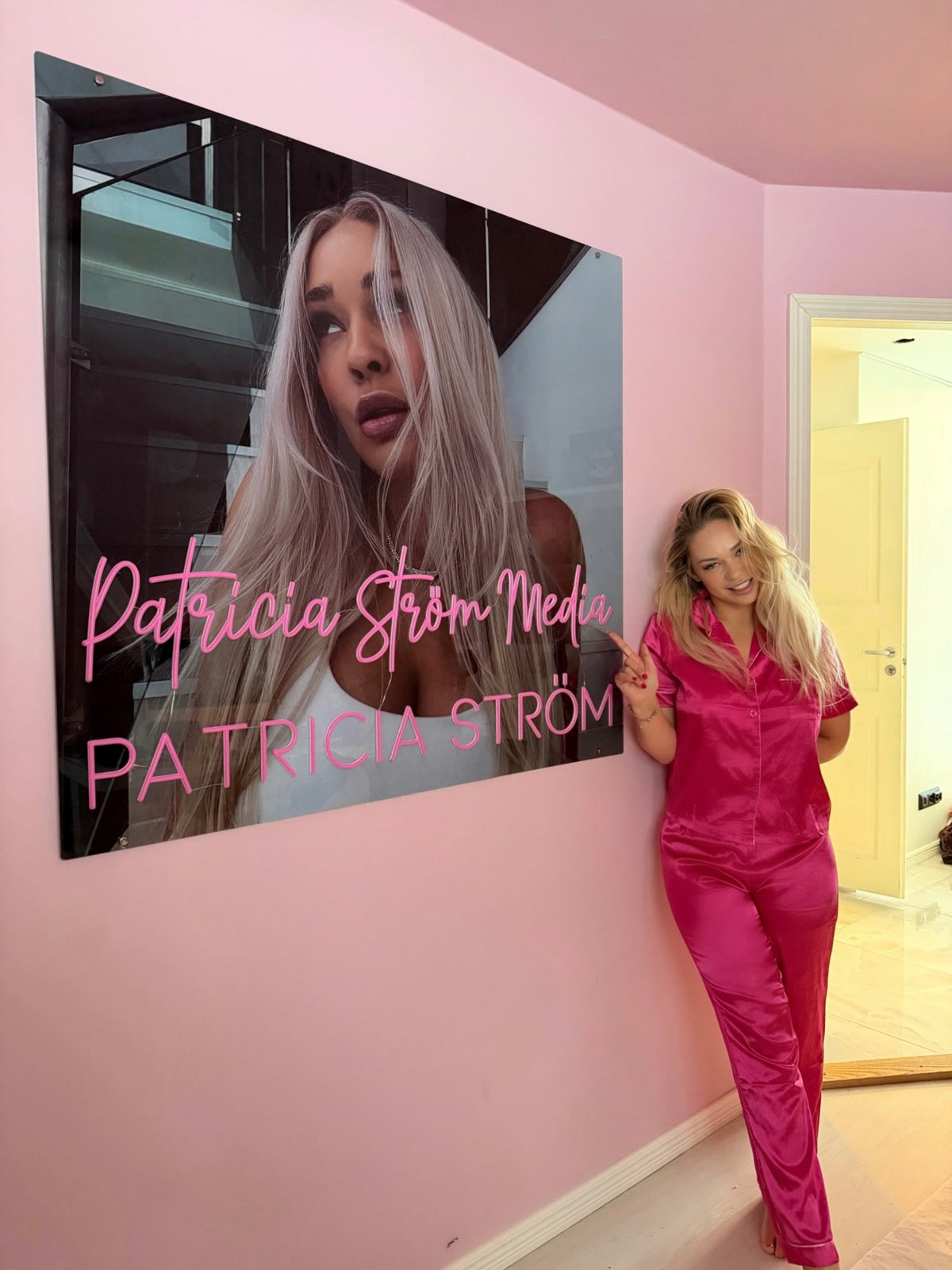 Růžové neonové logo Patricia Ström Media vystavené vedle Patricie Ström v jejím pracovním prostoru s identitou značky