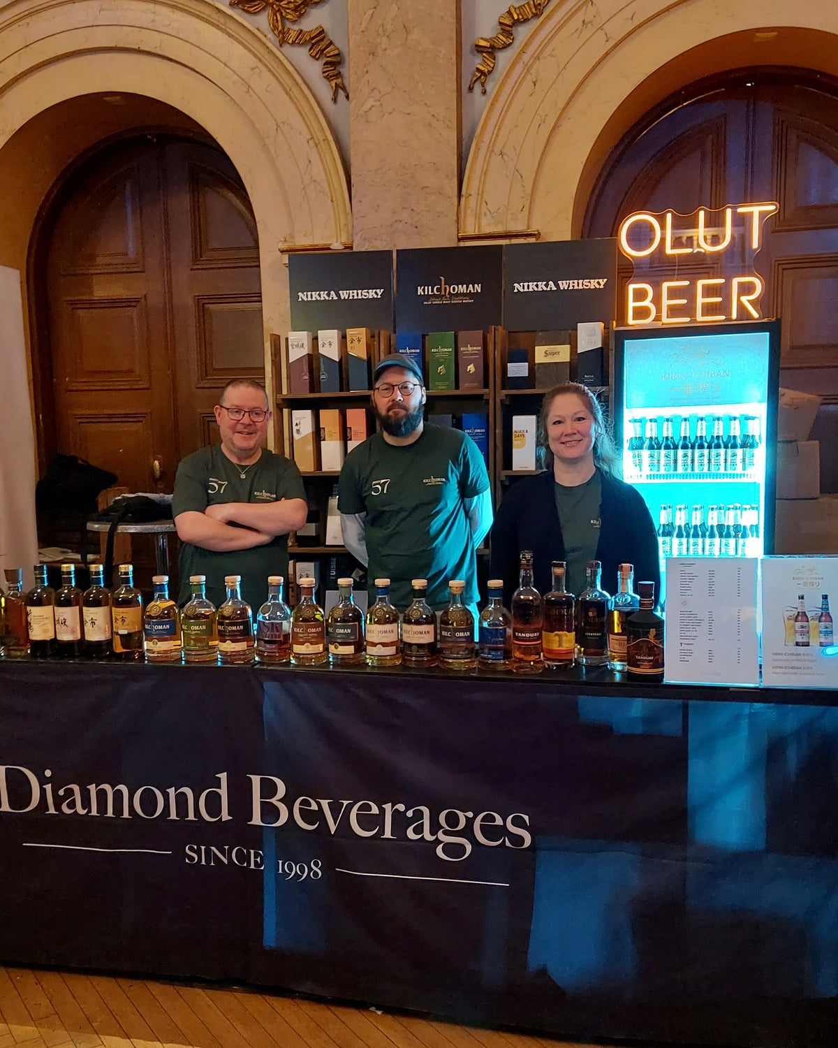 Text OLUT BEER z LED neonu v teplém odstínu nad degustačním stánkem Diamond Beverages.