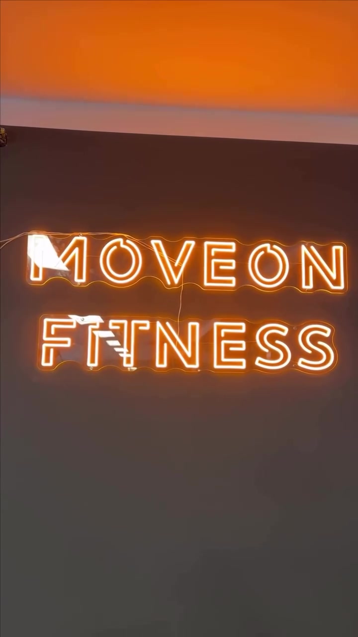 Sooja kollase LED-neooniga MOVEON FITNESS logo treeningstuudio tumedal seinal.