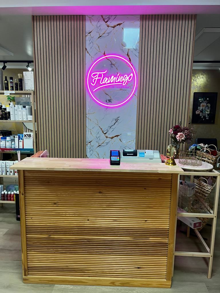 Růžové neonové logo Flamingo instalované za recepčním pultem v Parturi-Kampaamo Flamingo