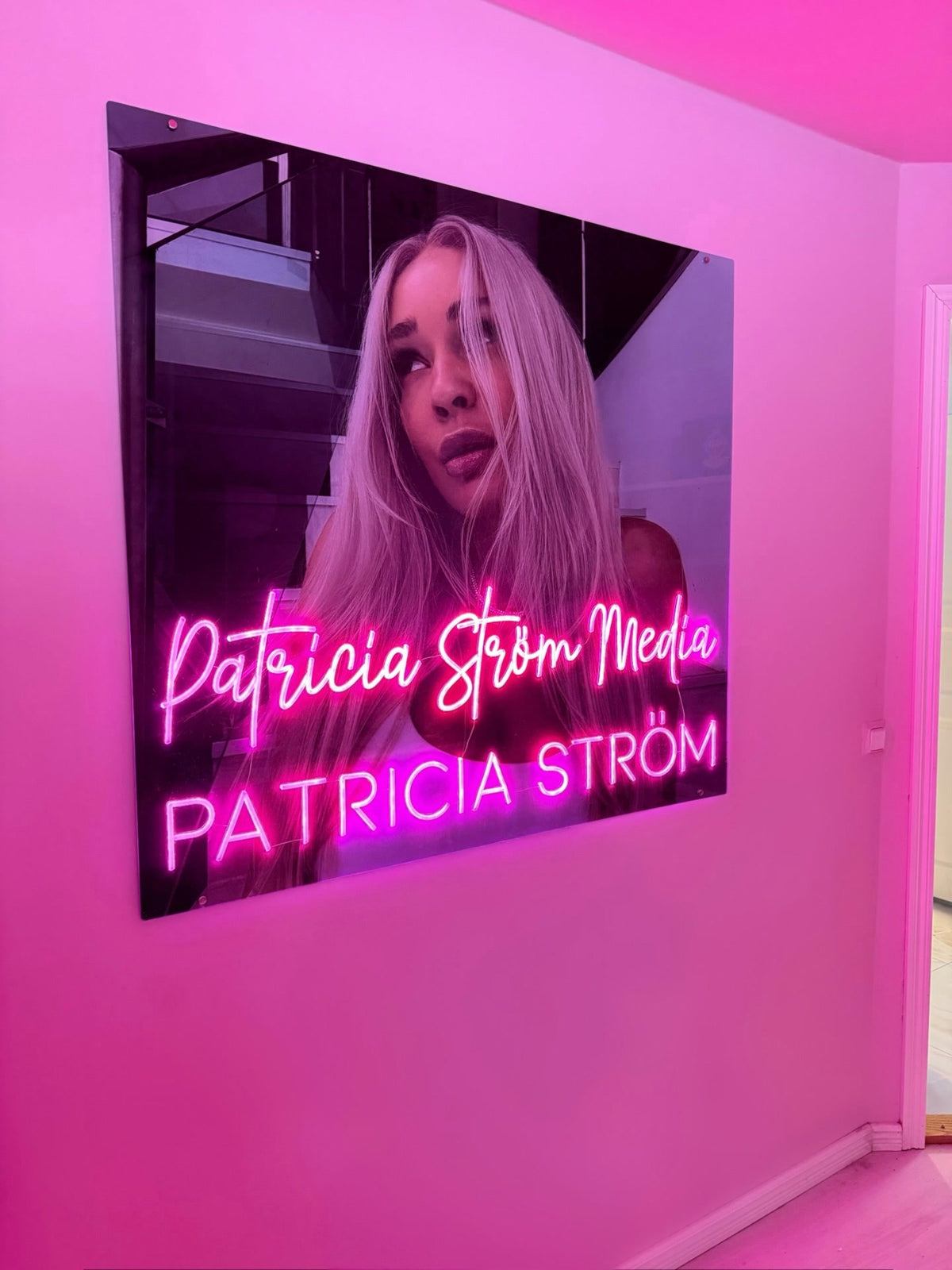 Růžové neonové logo Patricia Ström Media vystavené vedle Patricie Ström v jejím pracovním prostoru s identitou značky