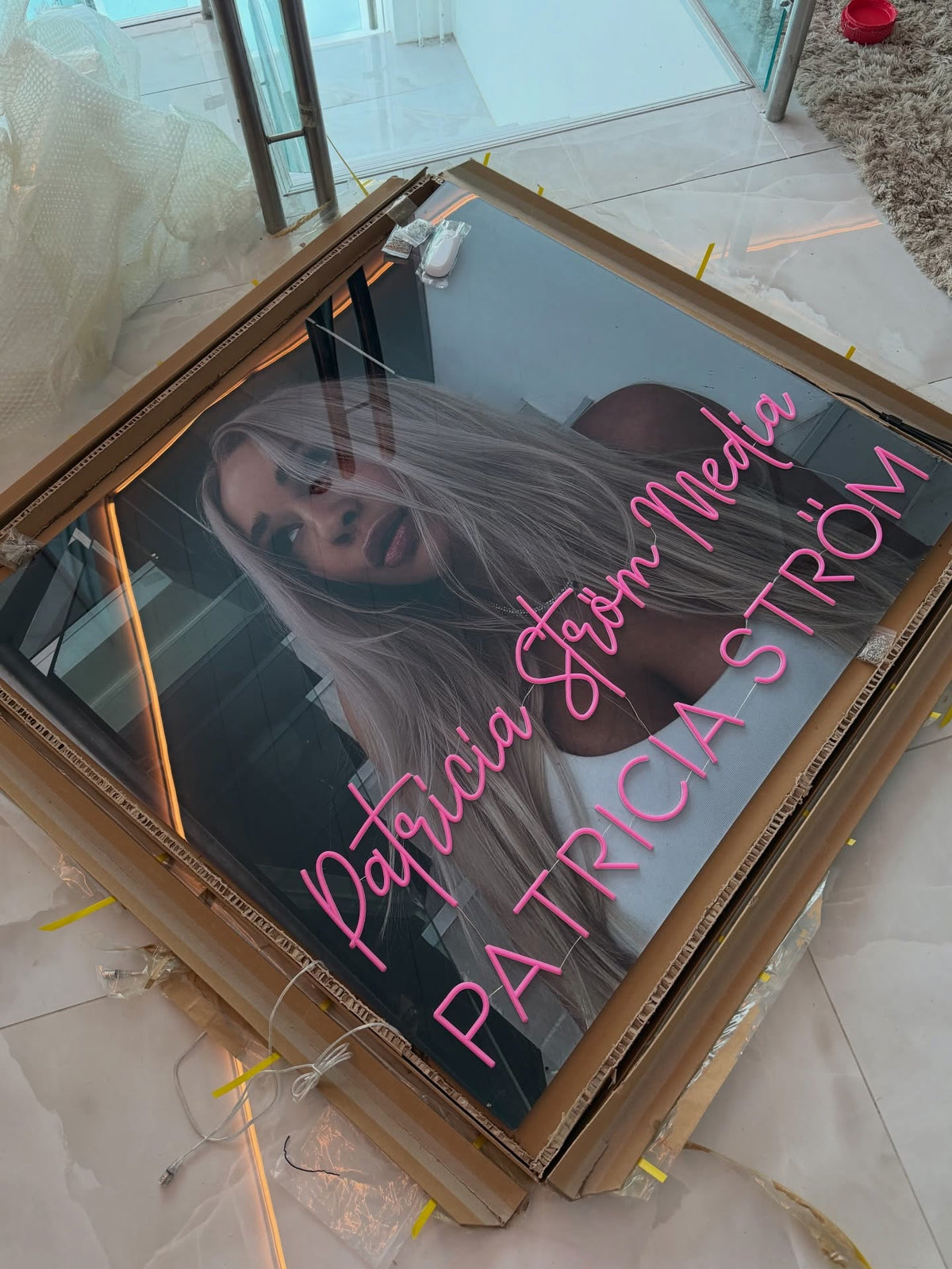 Růžové neonové logo Patricia Ström Media vystavené vedle Patricie Ström v jejím pracovním prostoru s identitou značky
