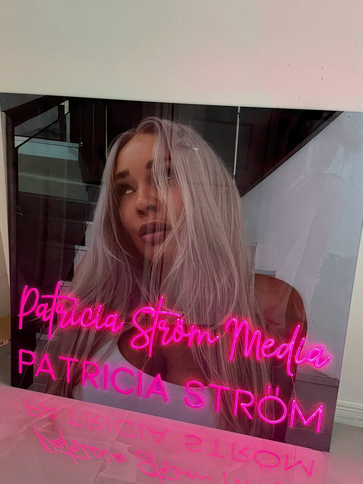 Růžové neonové logo Patricia Ström Media vystavené vedle Patricie Ström v jejím pracovním prostoru s identitou značky