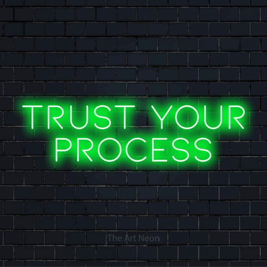 "Trust Your Process" glowing LED neon sign on a black brick wall